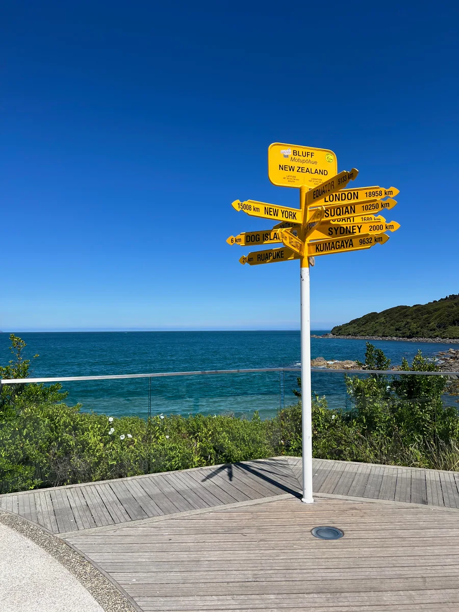 Yellow direction signs at Bluff pointing towards cities around the world above the sea