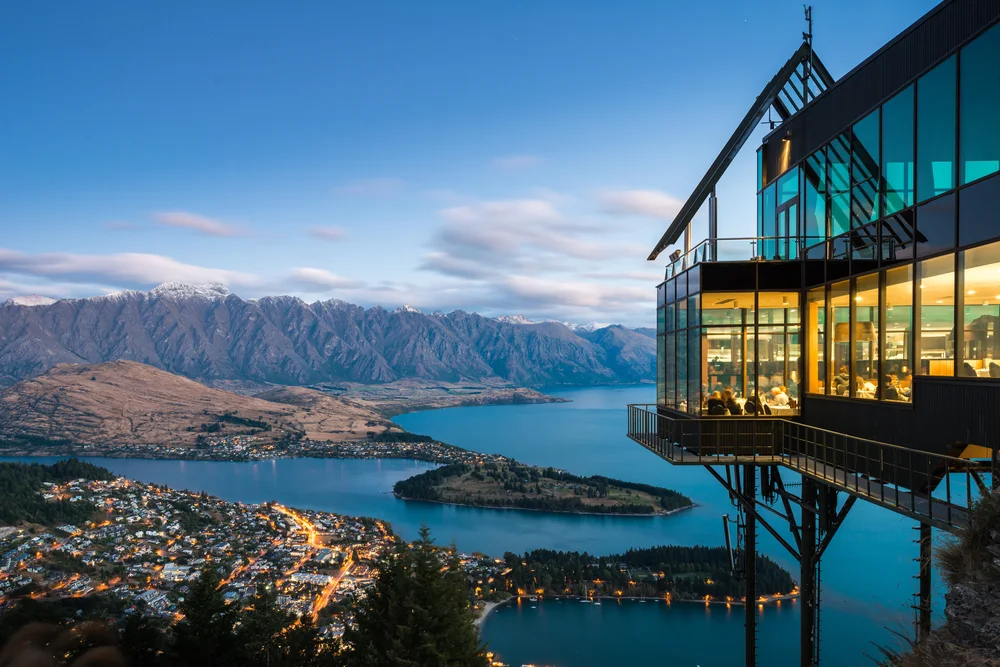 Queenstown and Lake Wakatipu at dusk, with the Remarkables beyond and a lit restaurant in the foreground